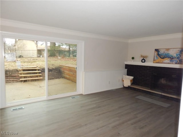 living area featuring a wainscoted wall, a fireplace, wood finished floors, visible vents, and crown molding