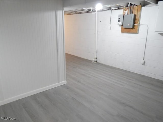 unfinished below grade area featuring concrete block wall, electric panel, baseboards, and wood finished floors