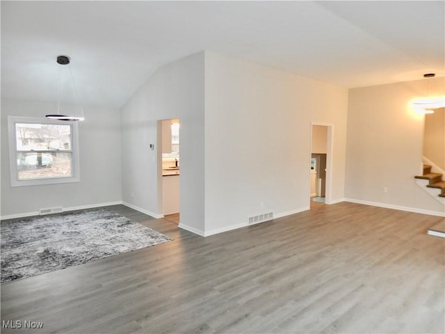 unfurnished living room featuring lofted ceiling, wood finished floors, visible vents, and stairs