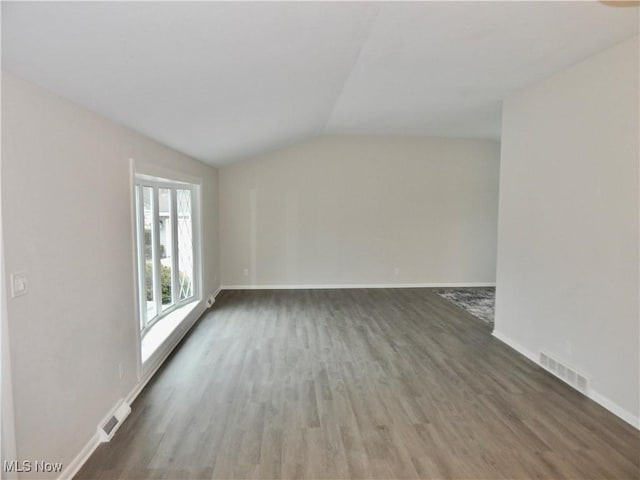 unfurnished room featuring visible vents, vaulted ceiling, baseboards, and wood finished floors