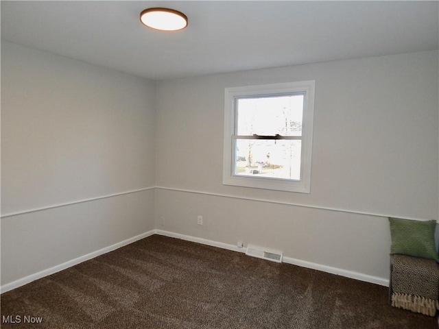 spare room with dark colored carpet, visible vents, and baseboards