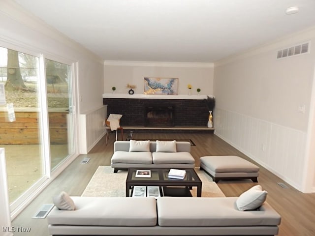 living area featuring a brick fireplace, wood finished floors, visible vents, and crown molding