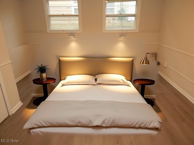 bedroom featuring multiple windows, baseboards, and wood finished floors