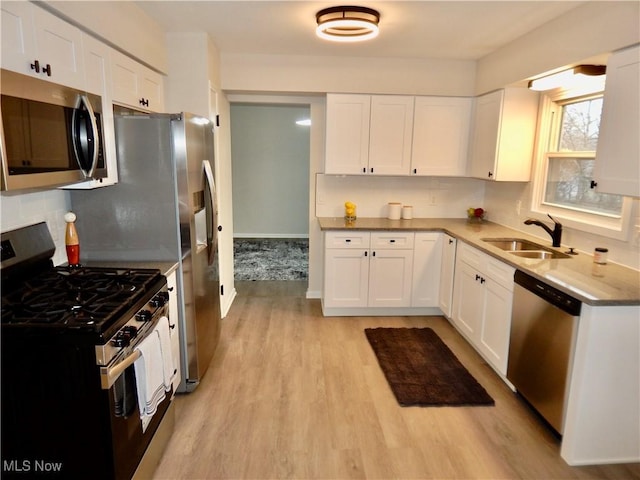 kitchen featuring light wood-style flooring, stainless steel appliances, a sink, white cabinets, and tasteful backsplash