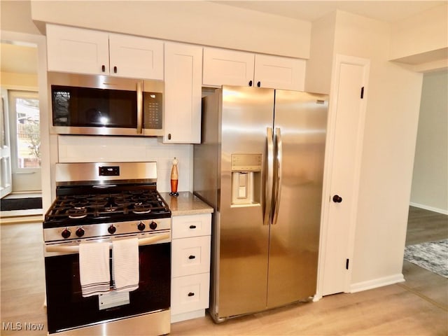 kitchen with appliances with stainless steel finishes, backsplash, white cabinetry, and light wood-style floors