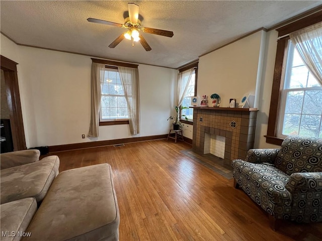 living room with a wealth of natural light, wood-type flooring, crown molding, and a tile fireplace