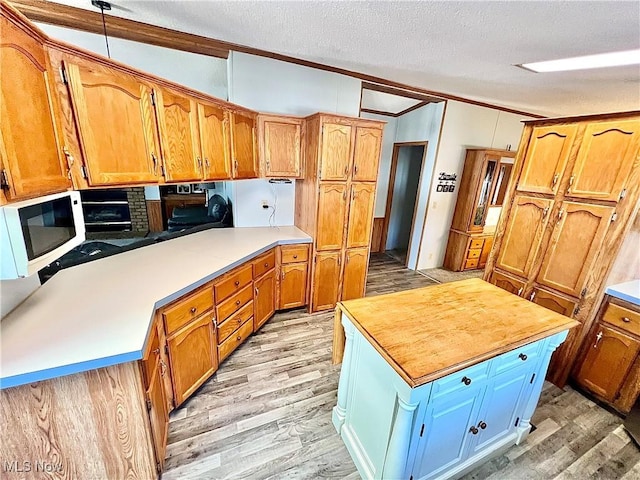 kitchen with brown cabinetry, white microwave, a center island, a textured ceiling, and light wood-type flooring