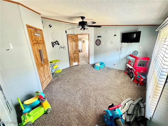 rec room featuring a textured ceiling, ceiling fan, carpet, and crown molding