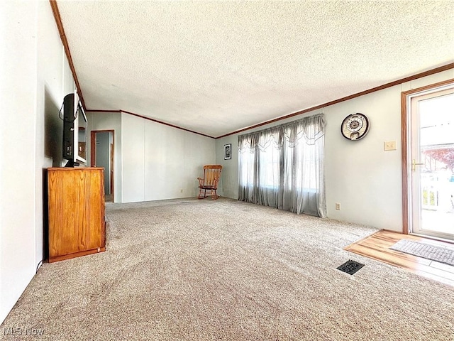 unfurnished living room with plenty of natural light, carpet, visible vents, and ornamental molding