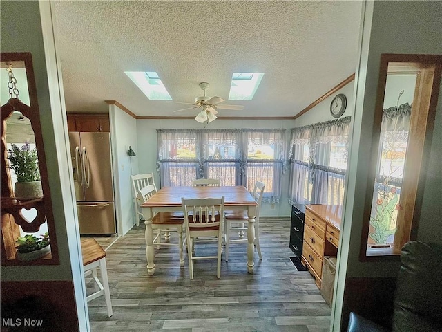 dining space featuring ornamental molding, ceiling fan, a textured ceiling, wood finished floors, and vaulted ceiling with skylight