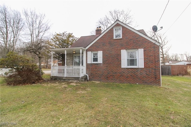 exterior space with brick siding, a chimney, a porch, a front yard, and fence