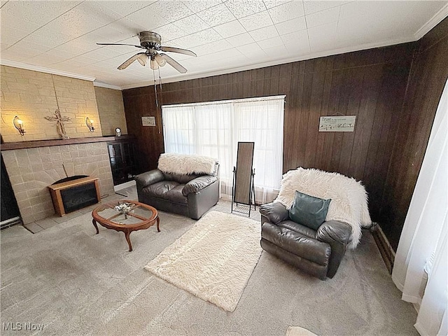 living area with carpet, a fireplace with flush hearth, wood walls, ornamental molding, and a ceiling fan