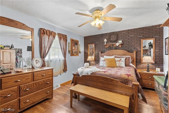 bedroom with light wood-style floors, visible vents, a textured ceiling, and brick wall