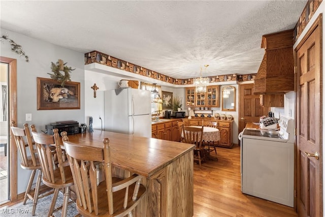 kitchen with light wood-style flooring, brown cabinetry, glass insert cabinets, washer / dryer, and white appliances