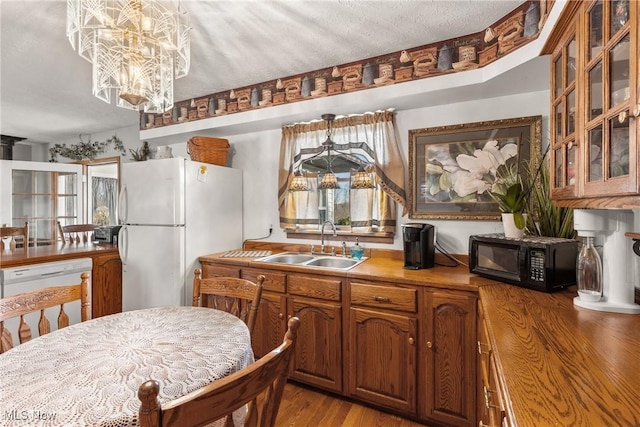 kitchen featuring white appliances, brown cabinetry, light wood-style flooring, glass insert cabinets, and a sink