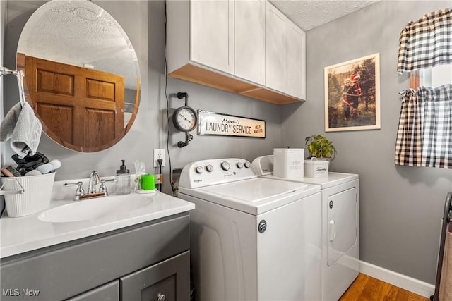 clothes washing area featuring a textured ceiling, a sink, baseboards, cabinet space, and washing machine and clothes dryer