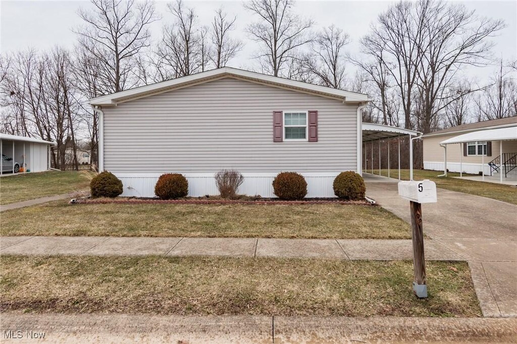 view of side of property featuring driveway, an attached carport, and a lawn