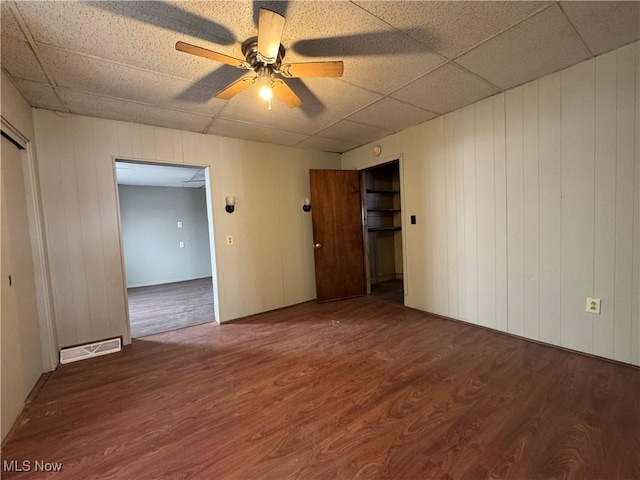 empty room featuring a paneled ceiling, a ceiling fan, visible vents, and wood finished floors