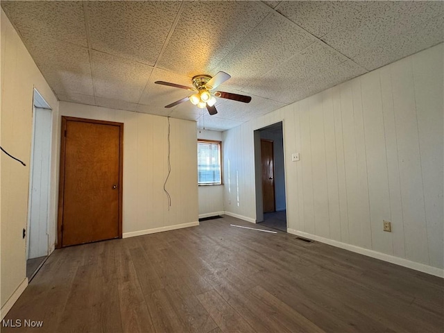 empty room with dark wood-type flooring, visible vents, baseboards, and a ceiling fan