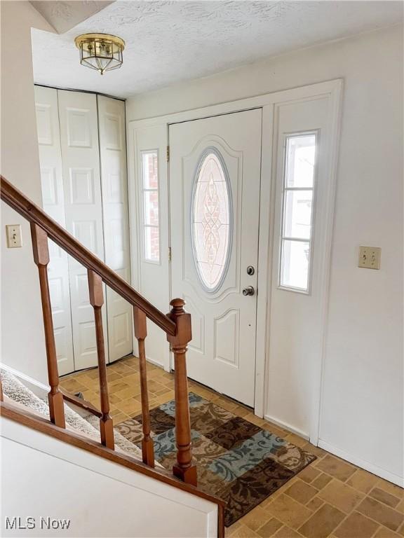 foyer featuring a healthy amount of sunlight, a textured ceiling, and stairs