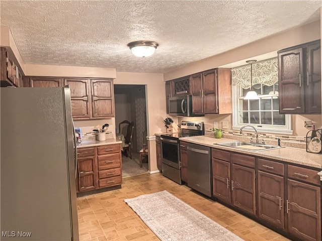 kitchen featuring pendant lighting, stainless steel appliances, light countertops, a sink, and a textured ceiling