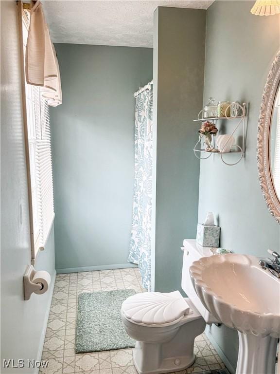 bathroom featuring a textured ceiling, a shower with curtain, toilet, and baseboards