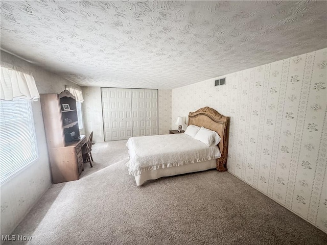 carpeted bedroom featuring wallpapered walls, visible vents, and a textured ceiling