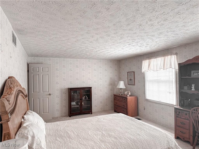 carpeted bedroom with a textured ceiling, visible vents, and wallpapered walls