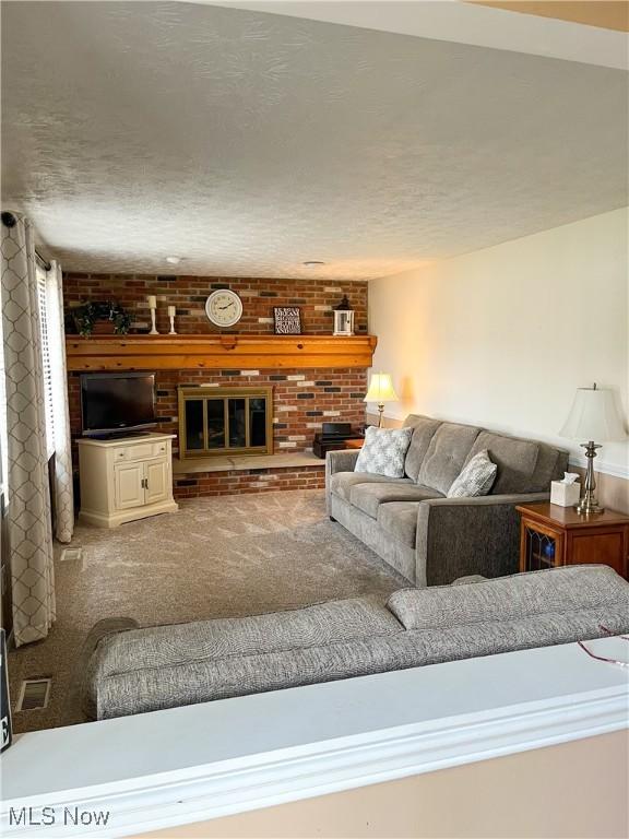 carpeted living room featuring visible vents, a fireplace, a textured ceiling, and brick wall