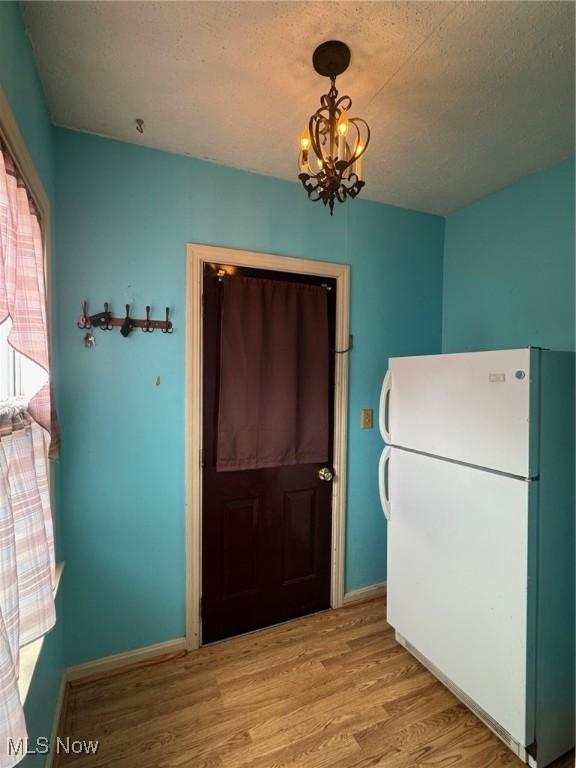 entryway featuring light wood finished floors, baseboards, a chandelier, and a textured ceiling