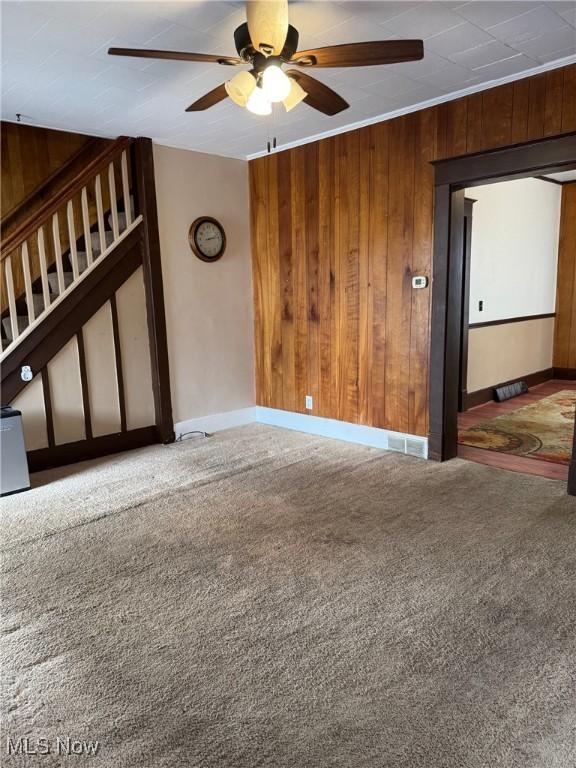 carpeted spare room featuring wood walls, stairs, baseboards, and a ceiling fan