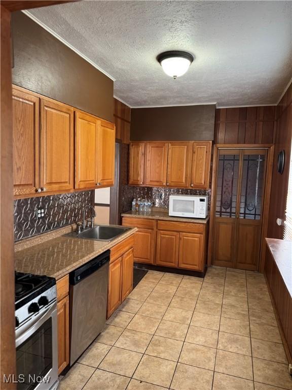 kitchen with appliances with stainless steel finishes, brown cabinets, a sink, and tasteful backsplash