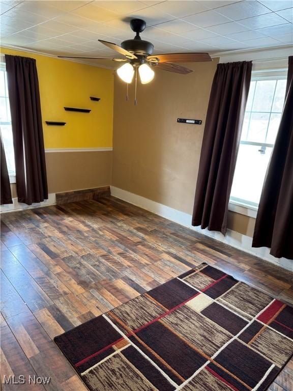 empty room with ornamental molding, a ceiling fan, baseboards, and wood finished floors