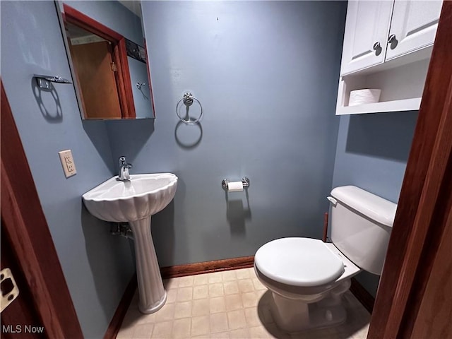 half bath with toilet, baseboards, and tile patterned floors