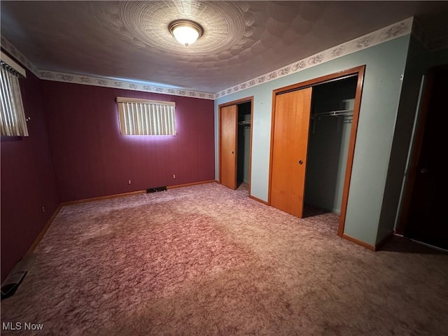 unfurnished bedroom featuring carpet flooring, two closets, visible vents, and baseboards