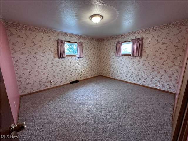 carpeted spare room featuring a wealth of natural light, a textured ceiling, baseboards, and wallpapered walls