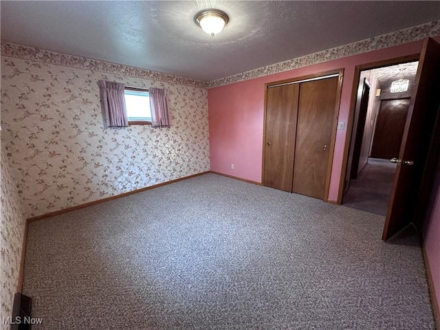 unfurnished bedroom with wallpapered walls, baseboards, a closet, and carpet flooring