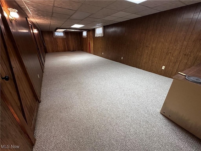 basement with carpet floors, wood walls, and a drop ceiling