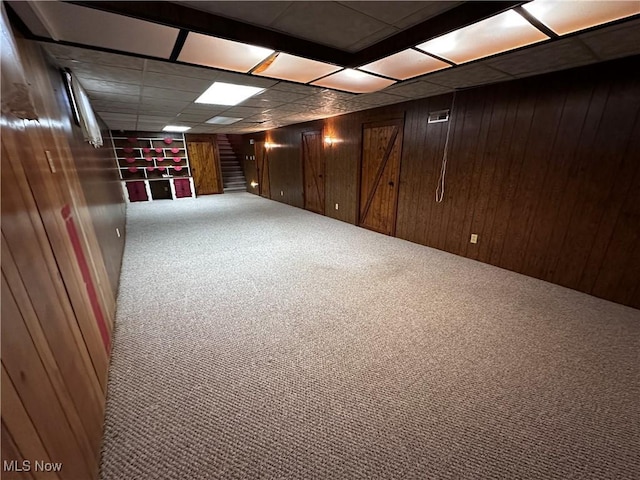 finished basement with a paneled ceiling, stairs, wooden walls, and carpet flooring