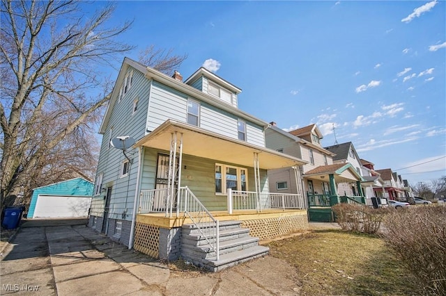 american foursquare style home with a detached garage, an outbuilding, a porch, and a chimney