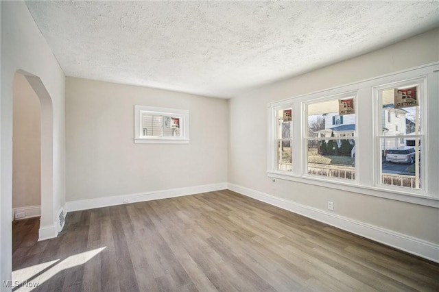 unfurnished room featuring wood finished floors, arched walkways, and baseboards