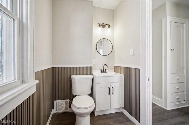 half bathroom featuring visible vents, toilet, wood finished floors, wainscoting, and vanity