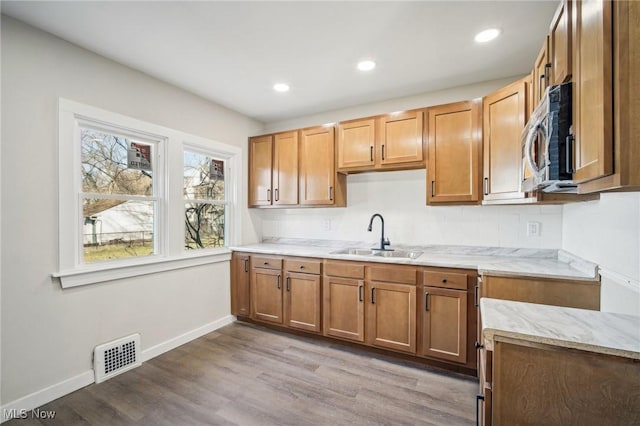 kitchen with stainless steel microwave, visible vents, light stone counters, wood finished floors, and a sink