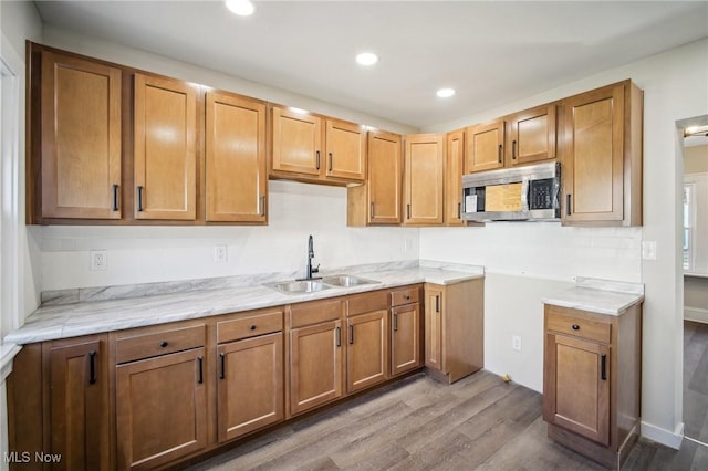 kitchen featuring brown cabinetry, wood finished floors, recessed lighting, a sink, and stainless steel microwave