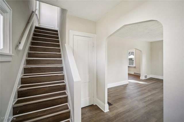 staircase featuring wood finished floors, arched walkways, and baseboards