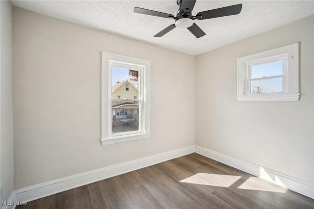 empty room with plenty of natural light, a textured ceiling, baseboards, and wood finished floors