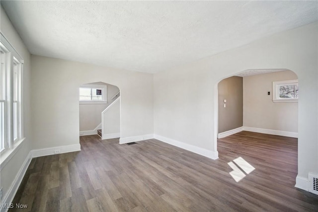 unfurnished room with a textured ceiling, wood finished floors, arched walkways, and baseboards