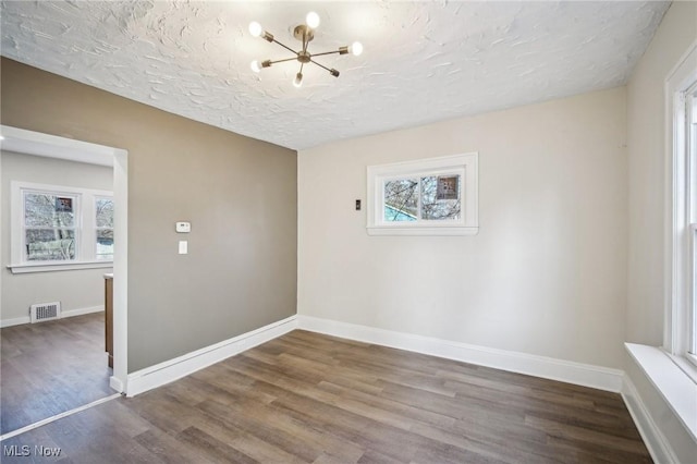 unfurnished room featuring visible vents, a textured ceiling, wood finished floors, baseboards, and a chandelier