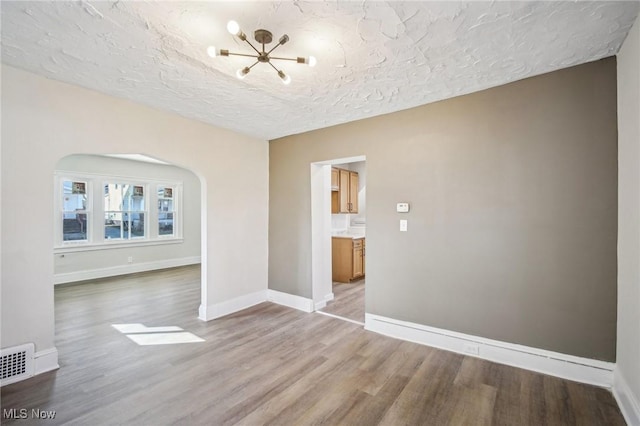 spare room featuring visible vents, baseboards, wood finished floors, arched walkways, and a textured ceiling