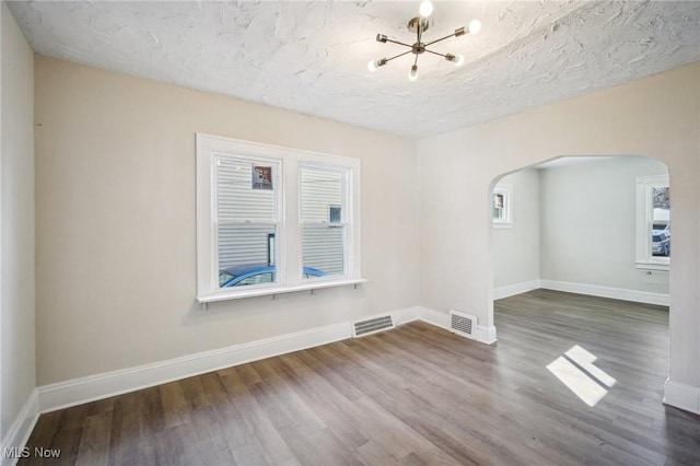 empty room featuring arched walkways, visible vents, baseboards, and wood finished floors